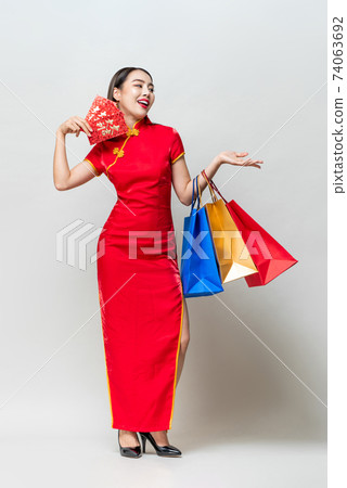 Asian woman in traditional dress holding bags and red evelelopes opening hand Asian woman in traditional dress holding bags and red evelelopes opening hand 74063692