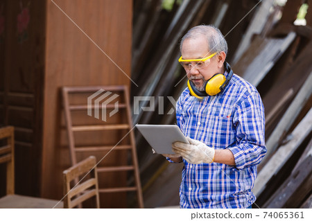 asian senior man carpenter wear headphone using tablet standing in workplace. carpenter concept. asian senior man carpenter wear headphone using tablet standing in workplace. carpenter concept. 74065361
