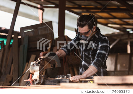 young carpenter man wear protective mask dust working use electronic saw cutting wood. 74065373