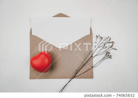 Blank white paper is placed on open brown paper envelope with red heart with Limonium dry flower on white background. Valentine's day concept. Blank white paper is placed on open brown paper envelope with red heart with Limonium dry flower on white background. Valentine's day concept. 74065632