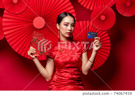 Beautiful Asian woman in qipao dress holding red envelopes and credit card Beautiful Asian woman in qipao dress holding red envelopes and credit card 74067459