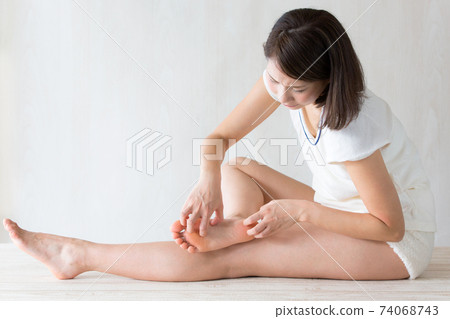 A woman scratching the soles of her feet. 74068743