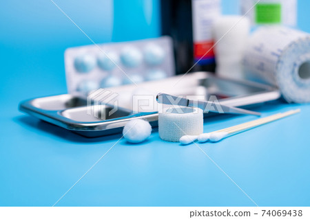 Wound care dressing set and stainless steel plate on blue background. Cotton ball, cotton stick, forceps and elastic cohesive retention bandage on blur wound care supplies. Medical equipment for nurse 74069438