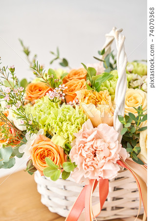 Small flower shop and Flowers delivery. Flower arrangement in Wicker basket. Beautiful bouquet of mixed flowers on wooden table. Handsome fresh bouquet. 74070368