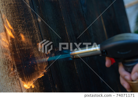 Professional carpenter using old traditional japanese technique. Burning wood planks with gas burner Professional carpenter using old traditional japanese technique. Burning wood planks with gas burner 74071171
