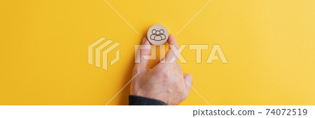 Male hand placing wooden cut circle with people symbol on it on yellow background Male hand placing wooden cut circle with people symbol on it on yellow background 74072519