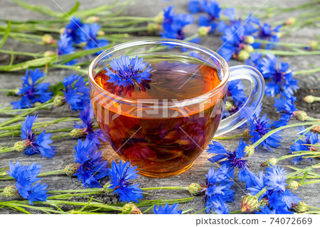 Cup of herbal tea and blue cornflowers flowers on wood background. 74072669