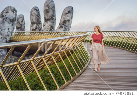 Young woman tourist at Famous tourist attraction - Golden bridge at the top of the Ba Na Hills, Vietnam Young woman tourist at Famous tourist attraction - Golden bridge at the top of the Ba Na Hills, Vietnam 74075881