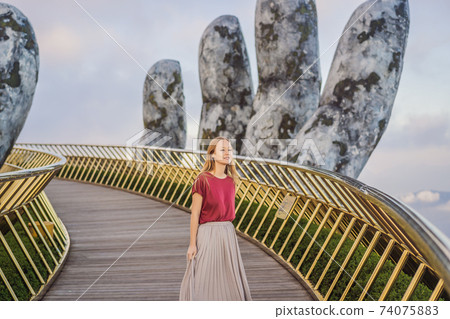 Young woman tourist at Famous tourist attraction - Golden bridge at the top of the Ba Na Hills, Vietnam Young woman tourist at Famous tourist attraction - Golden bridge at the top of the Ba Na Hills, Vietnam 74075883