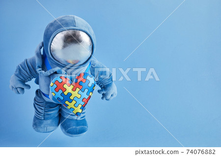 World Autism awareness day background. Blue plush astronaut toy with puzzle heart, autism symbol, on blue background World Autism awareness day background. Blue plush astronaut toy with puzzle heart, autism symbol, on blue background 74076882