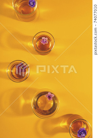 Glass cups of tea with flowers on bright yellow with shadows 74077010