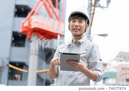 在建築地盤工作的頭盔的年輕工人 74077874