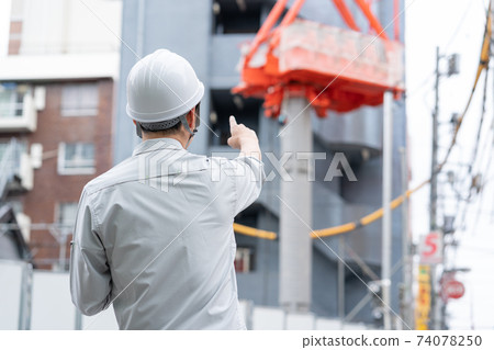 Back view of a young worker wearing a helmet working at a construction site 74078250