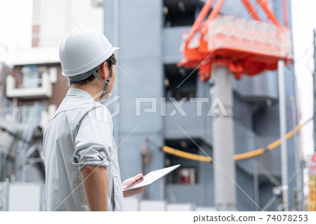 Back view of a young worker wearing a helmet working at a construction site 74078253