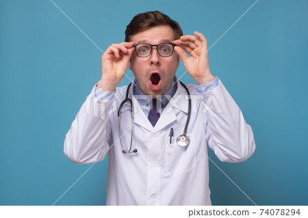 Hispanic adult man wearing doctor uniform and stethoscope with surprise and amazed expression on face. Hispanic adult man wearing doctor uniform and stethoscope with surprise and amazed expression on face. 74078294