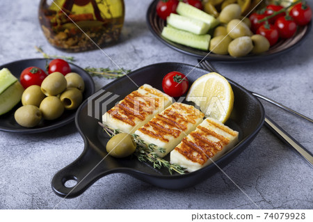 Grilled haloumi cheese on a black pan with olives, tomatoes, cucumbers and pepperoni. Close-up. Grilled haloumi cheese on a black pan with olives, tomatoes, cucumbers and pepperoni. Close-up. 74079928