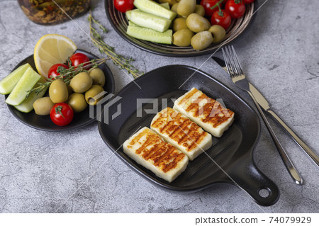 Grilled haloumi cheese on a black pan with olives, tomatoes, cucumbers and pepperoni. Close-up. Grilled haloumi cheese on a black pan with olives, tomatoes, cucumbers and pepperoni. Close-up. 74079929