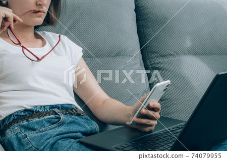 Young woman checking phone - using both laptop and smartphone. Social network, online safety and digital lockdown in USA concept. Internet censorship. Selective focus 74079955