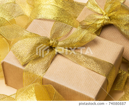 gift wrapped in brown paper on a twisted golden ribbon background, festive background, top view gift wrapped in brown paper on a twisted golden ribbon background, festive background, top view 74080887