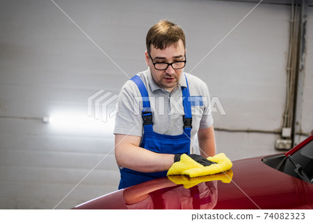 Man cleans car surface from drops using wiper. Man cleans car surface from drops using wiper. 74082323