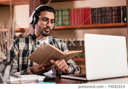 Arab Student Learning Reading Book Sitting At Laptop In Library Arab Student Learning Reading Book Sitting At Laptop In Library 74082814