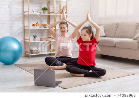 Stay home workout. Millennial mother with teen daughter doing yoga practice to online video on laptop in living room 74082968