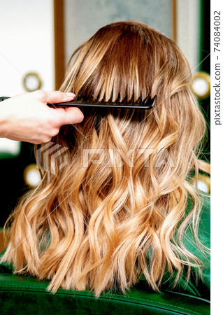 Hairdresser combing wavy hair of woman 74084002
