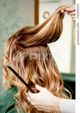 Hairdresser holds strand of hair 74084003