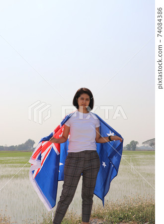 pretty lady in white shirt with Australia flag on her shoulder on nature view background. 74084386