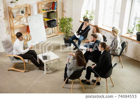 Male speaker giving presentation in hall at workshop. Audience or conference hall. High angle view of unrecognized participants. Male speaker giving presentation in hall at workshop. Audience or conference hall. High angle view of unrecognized participants. 74084553