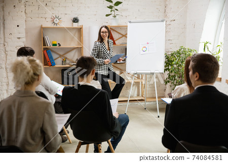 Female speaker giving presentation in hall at workshop. Audience or conference hall. Rear view of unrecognized participants. 74084581
