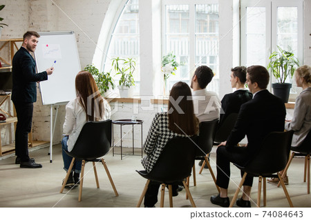Male speaker giving presentation in hall at workshop. Audience or conference hall. Rear view of unrecognized participants. 74084643