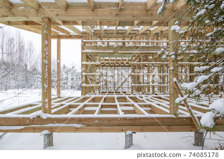frame house construction in winter, under the snow, in the forest. Fresh wood, frame of a two-story house 74085178