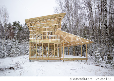 frame house construction in winter, under the snow, in the forest. Fresh wood, frame of a two-story house frame house construction in winter, under the snow, in the forest. Fresh wood, frame of a two-story house 74085188