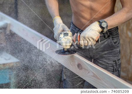 sanding the board with a hand-held power tool. Street, board clamped in a vise, small sawdust. sanding the board with a hand-held power tool. Street, board clamped in a vise, small sawdust. 74085209