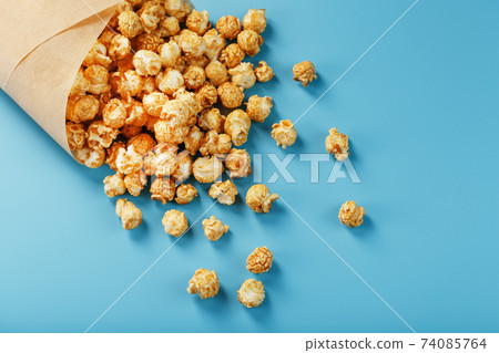 Popcorn in caramel glaze in a paper envelope on a blue background. Popcorn in caramel glaze in a paper envelope on a blue background. 74085764
