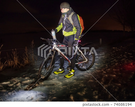 Extreme biker stopped winter riding and drinks a refreshing drink  in night. 74086194