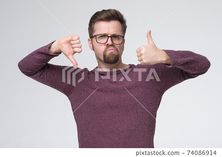Caucasian man does not know what to choose, showing thumb up and down. Caucasian man does not know what to choose, showing thumb up and down. 74086914