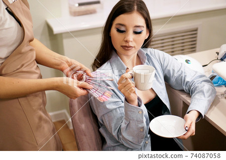 The manicurist demonstrates to client the palettes with the color of the nails The manicurist demonstrates to client the palettes with the color of the nails 74087058