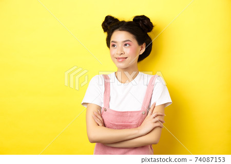 Smiling beautiful asian girl with glamour makeup, looking aside at logo with happy face, standing in summer clothes on yellow background Smiling beautiful asian girl with glamour makeup, looking aside at logo with happy face, standing in summer clothes on yellow background 74087153