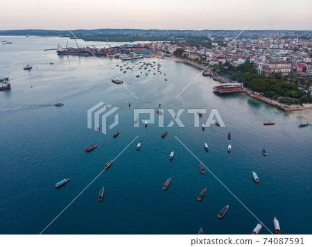 Aerial. Stone town, Zanzibar, Tanzania. Flock of Show Ships near the Zanzibar Coastline in Stone Town on Blue Transparent Water Aerial. Stone town, Zanzibar, Tanzania. Flock of Show Ships near the Zanzibar Coastline in Stone Town on Blue Transparent Water 74087591