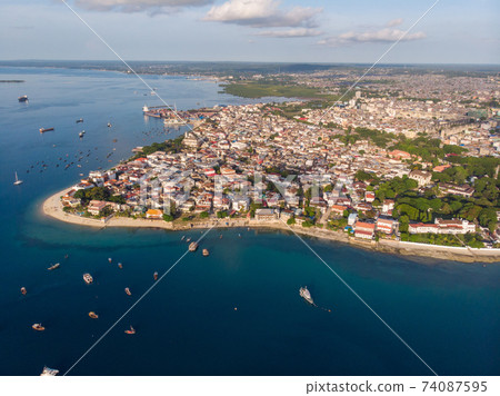 Aerial. Stone town, Zanzibar, Tanzania. Flock of Show Ships near the Zanzibar Coastline in Stone Town on Blue Transparent Water Aerial. Stone town, Zanzibar, Tanzania. Flock of Show Ships near the Zanzibar Coastline in Stone Town on Blue Transparent Water 74087595