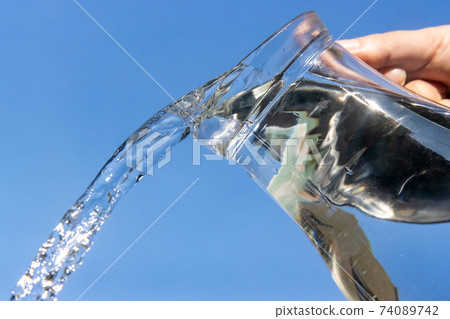 A Clear water flowing from a glass jug on a blue background. 74089742