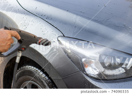 Manual car wash with pressurized water. Cleaning front part of car with high pressure water. Manual car wash with pressurized water. Cleaning front part of car with high pressure water. 74090335