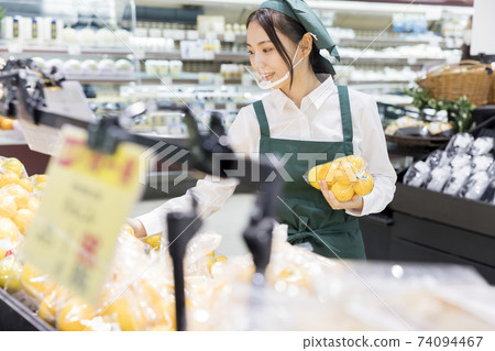 A female employee with a mouth shield who puts out goods at a supermarket 74094467