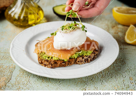 Home-made toast with mashed avocado, salmon, poached egg and microgreens 74094943