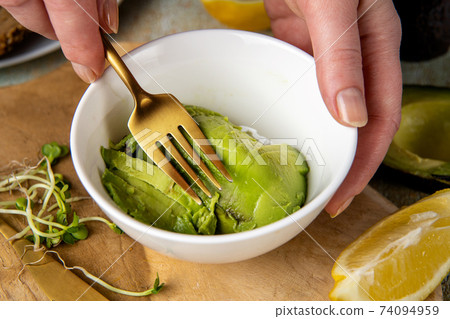 Female hands mashing with a fork avocado in white plate Female hands mashing with a fork avocado in white plate 74094959