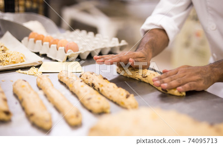 Male baker working with dough forming baguettes 74095713