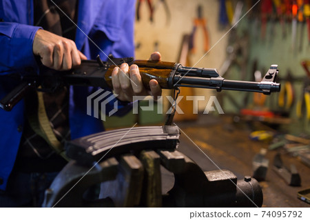 Kalashnikov assault rifle in hands of gunsmith in weapons workshop 74095792