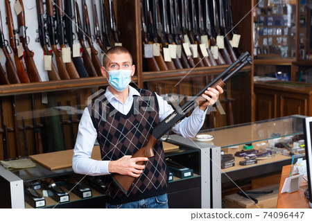 Gun shop salesman in mask offering pump action hunting rifle Gun shop salesman in mask offering pump action hunting rifle 74096447